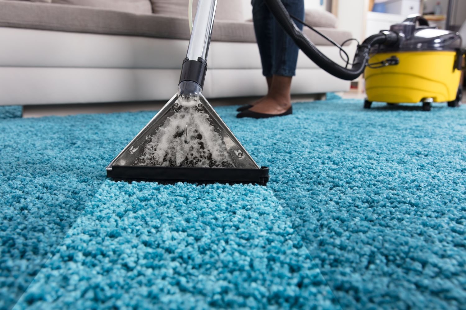 Woman using a vacuum cleaner on a blue carpet, representing a rug cleaning service in Chicago, IL.