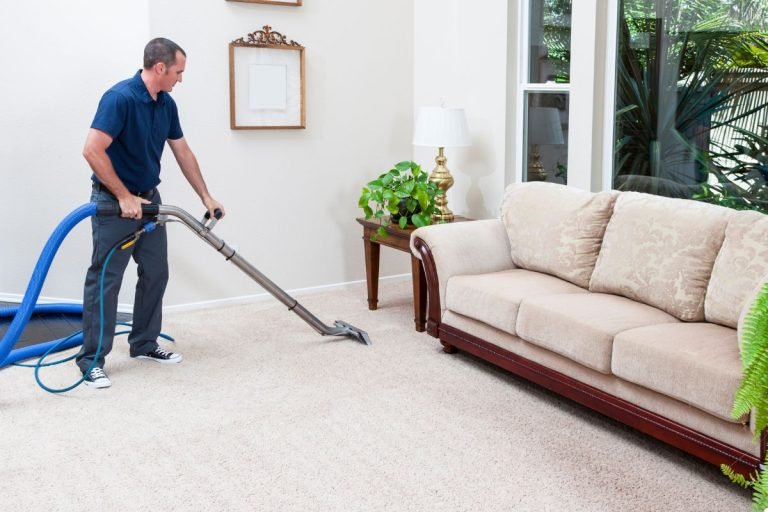 A man using a vacuum cleaner to clean the carpet in a tidy living room filled with furniture and decor.