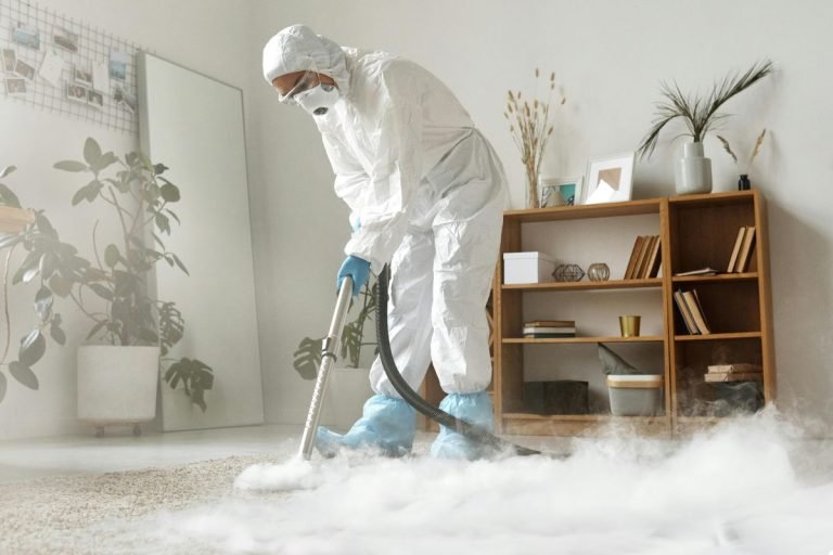 A man wearing protective clothing and a mask cleans a room, ensuring a safe and sanitized environment.