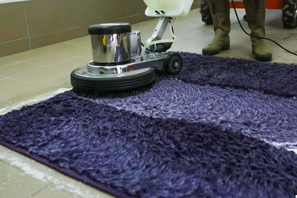 A person using a cleaning machine on a purple rug, focusing on removing dirt and stains from the fabric.