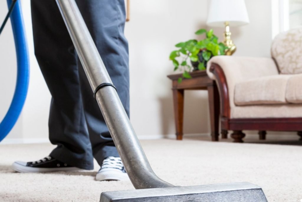 A person using a vacuum cleaner to clean a carpet in a well-lit room, focusing on removing dirt and debris.